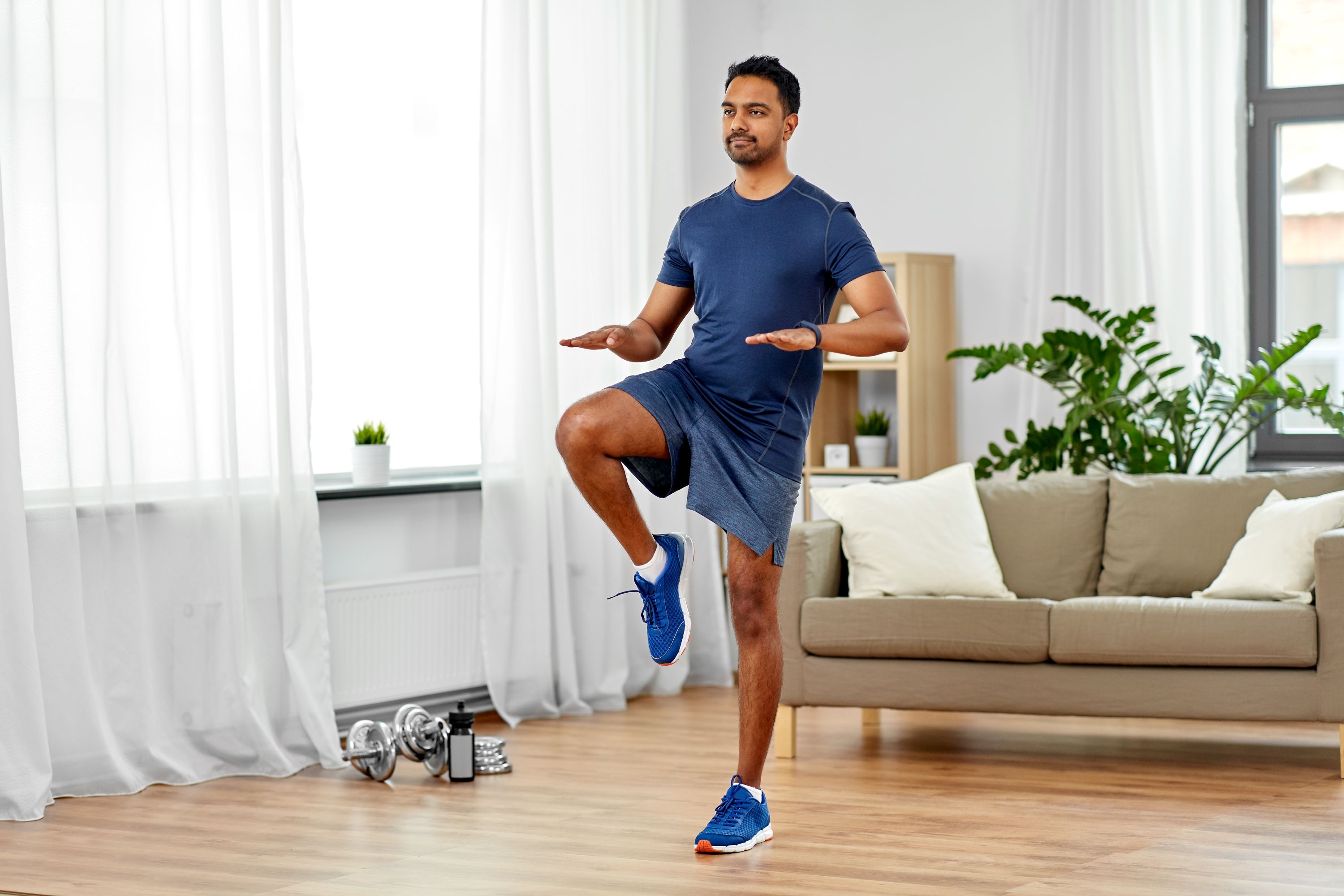 Young asian man running on the spot wearing a t-shirt and shorts in their living room on a wooden floor.